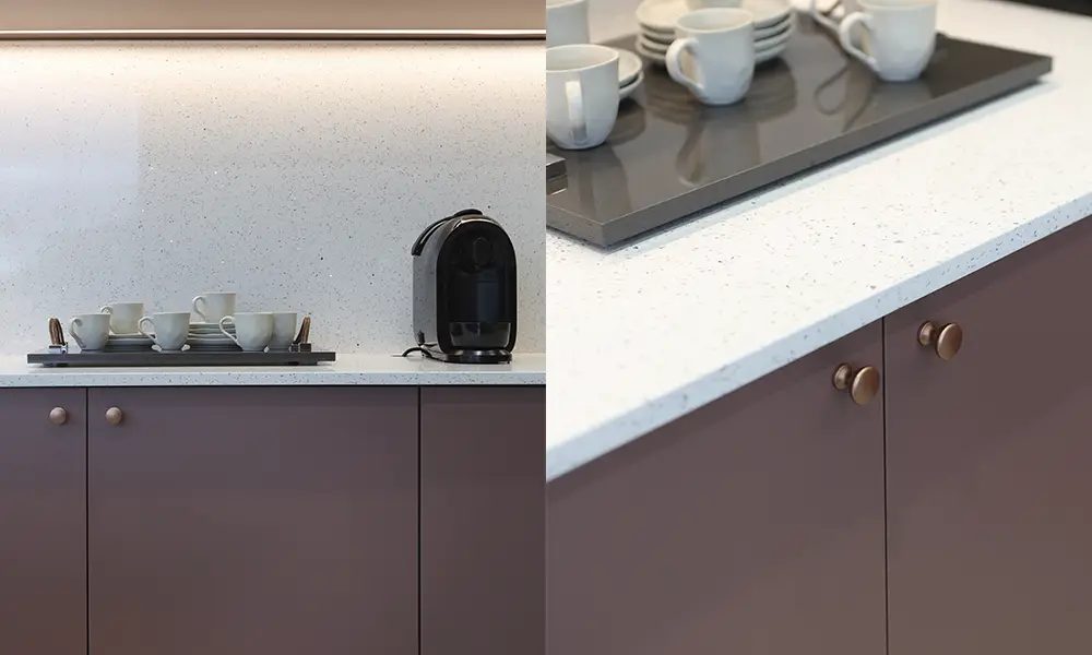 Close-up de bancada de cozinha moderna com superfície branca texturizada, armários inferiores em tom terracota e acessórios como bandeja com xícaras e máquina de café.